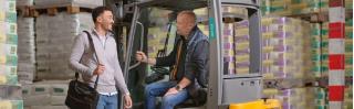 man in heftruck praat met adviseur in magazijn met veel voorraad